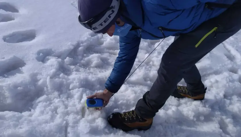 Persona en la arva montaña, con equipo de rescate, buscando algo en la nieve.