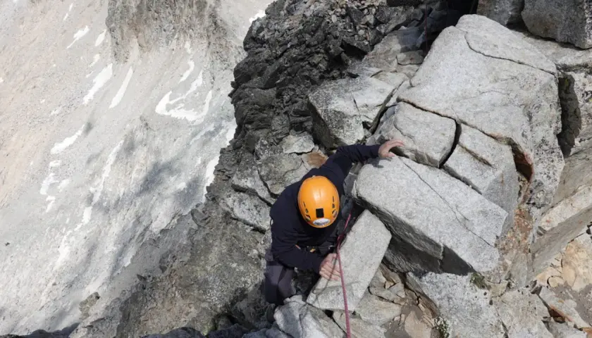 Alpinista con casco naranja escala roca, buscando el aneto por coronas.