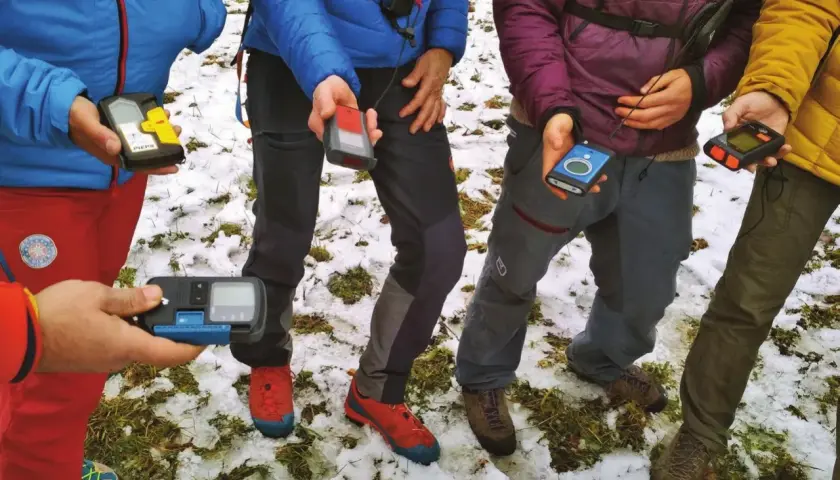 Personas en la nieve sostienen varios dispositivos de búsqueda de avalanchas, como el PIEPS, para una lección de seguridad en montaña.