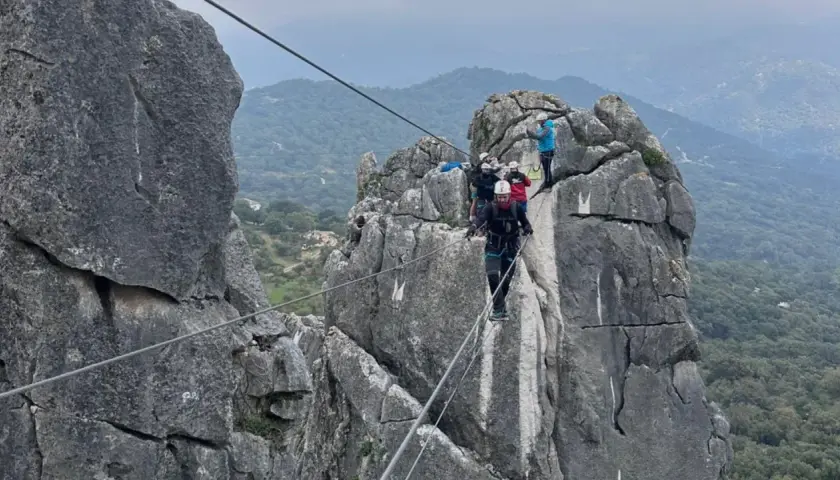 Grupo de personas superando diferentes niveles de vía ferrata, asegurados a cables de acero sobre rocas escarpadas.