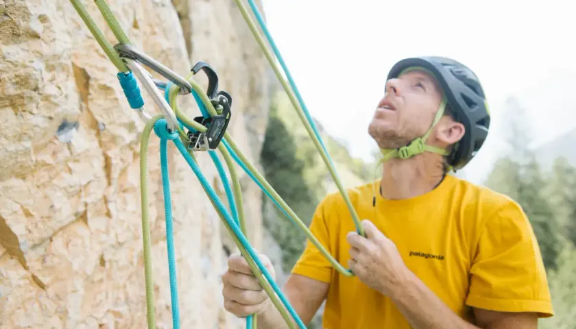 Escalador con casco y camiseta amarilla, asegurando cuerdas de escalada. La **cesta escalada** está lista para la aventura.