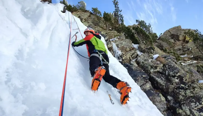Escalador en hielo en los Pirineos, disfrutando de corredores fáciles con crampones y piolet.