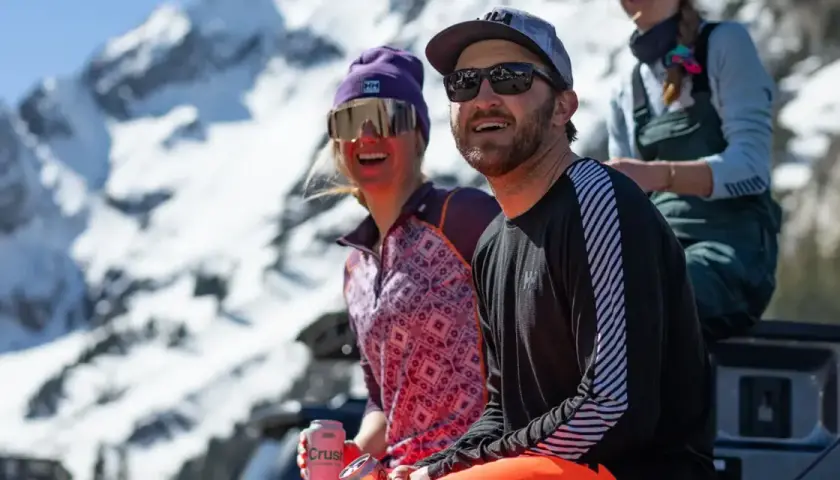 Dos amigos disfrutan del sol en la montaña, abrigados con ropa de poliamida.