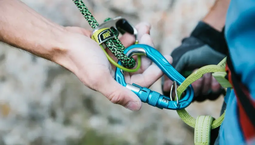 Manos ajustando cuerda y mosquetones azules, esenciales para escalada. Los mejores mosquetones garantizan seguridad.