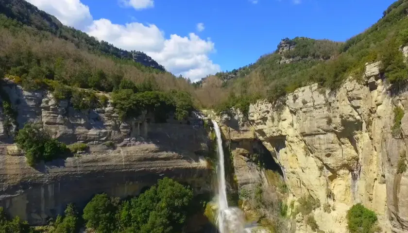 Cascada impresionante en un cañón rocoso, ideal para senderismo en Cataluña. El agua cae en una cortina blanca sobre la piedra dorada.