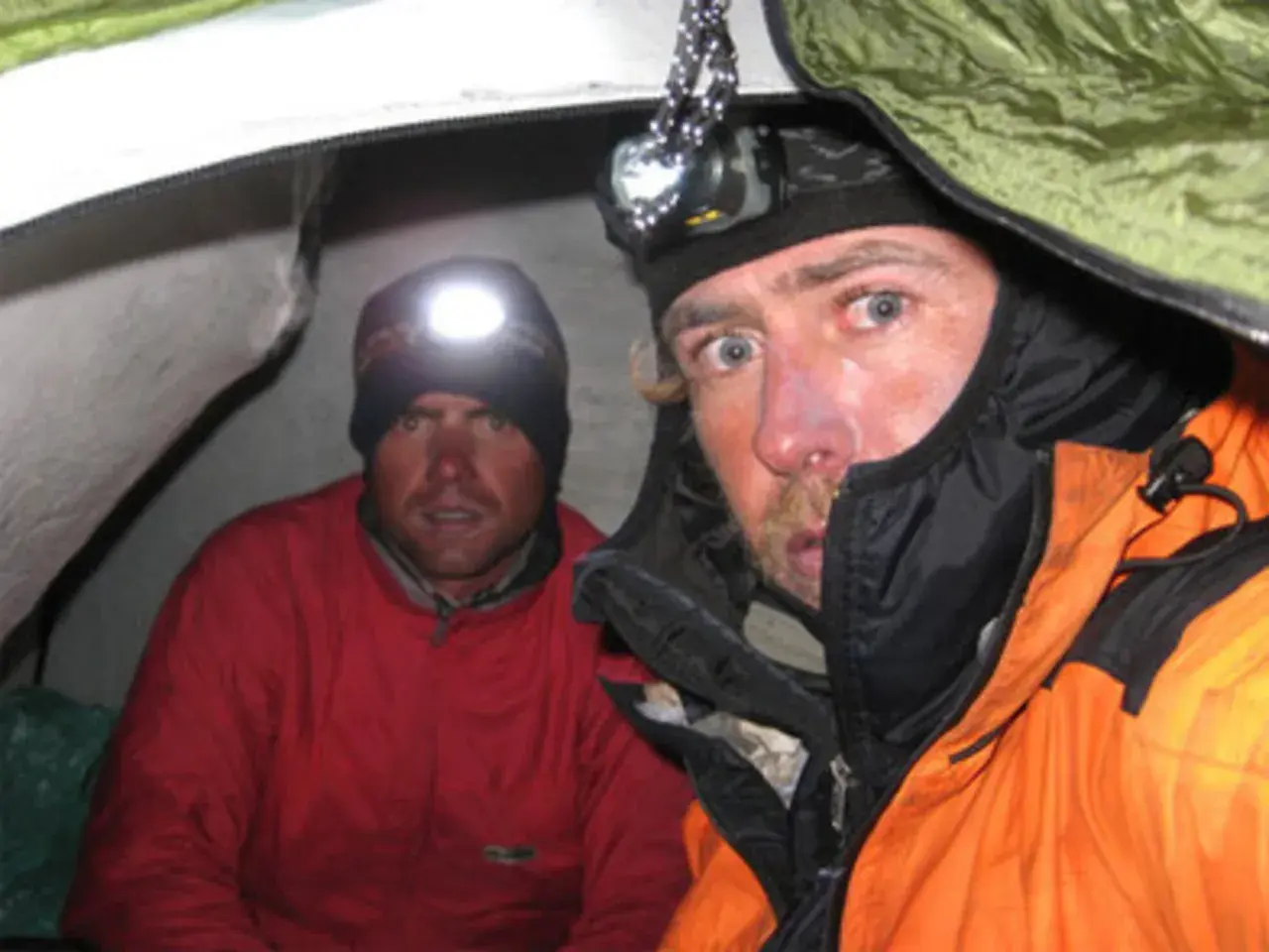 Oscar Pérez, alpinista, y su compañero en una tienda de campaña, ambos con linternas frontales encendidas.