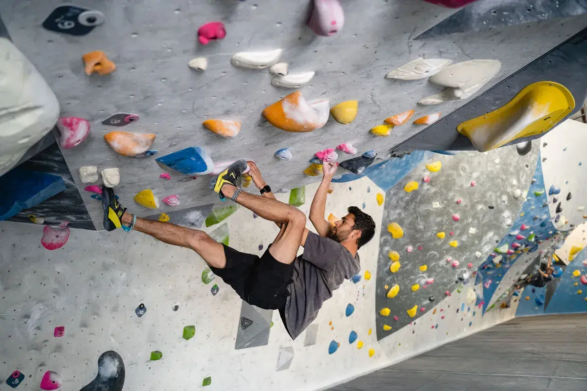 Hombre escalando en un rocódromo interior, superando diferentes grados escalada boulder con agarres de colores.