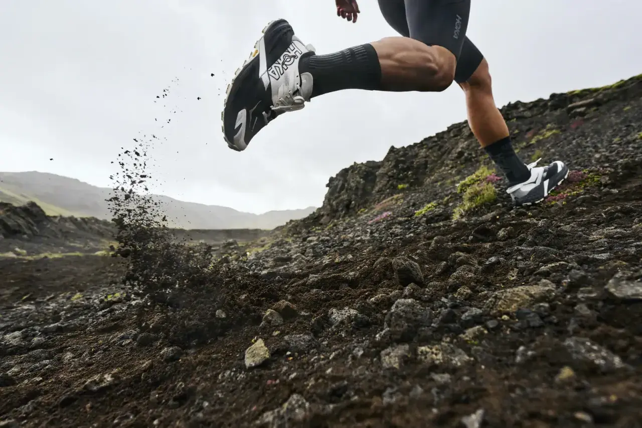 Corredor en terreno rocoso, levantando tierra con su zapatilla Hoka equipada con suela Vibram Megagrip.