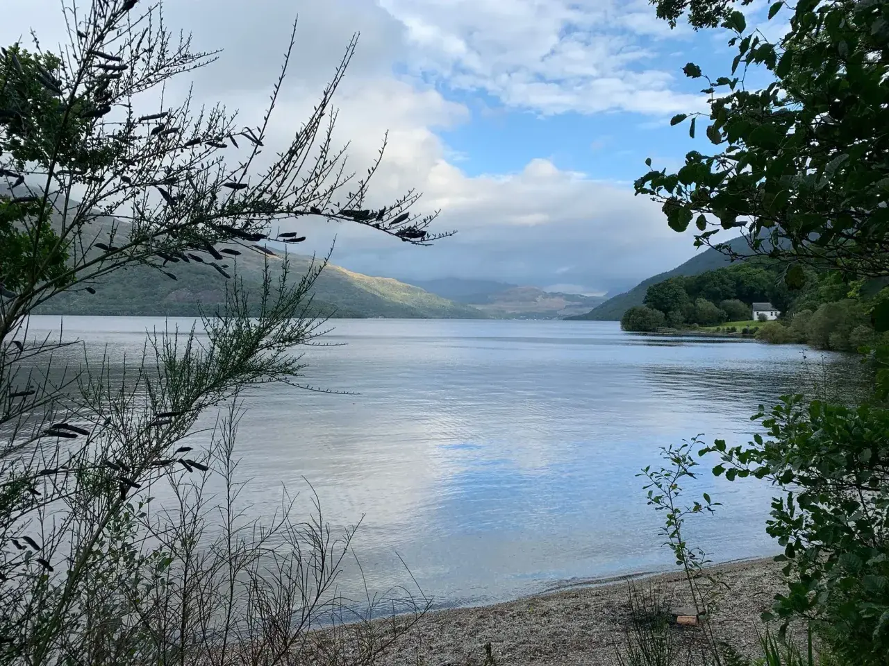 Un lago sereno en el West Highland Way, con colinas cubiertas de vegetación y un cielo nublado.