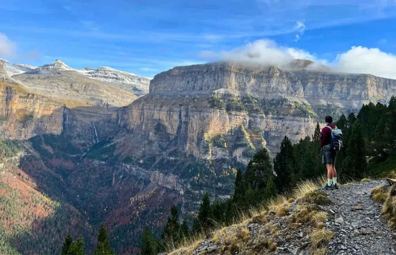 Senderista admira imponentes acantilados y cascadas en las rutas Pirineos. El otoño tiñe el valle de colores cálidos.