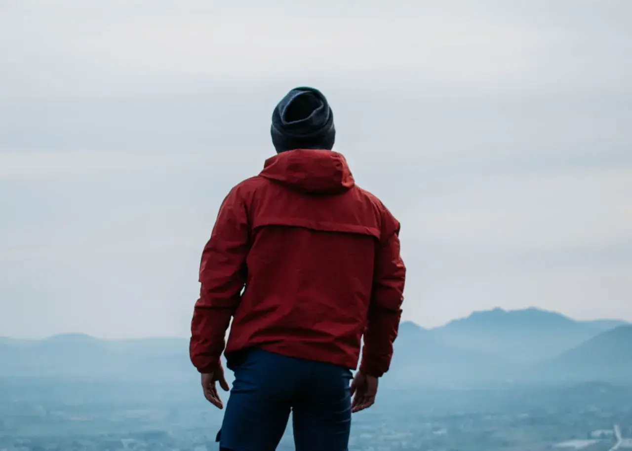 Hombre con chaqueta roja y gorro azul, contemplando el paisaje. ¿Primoloft vs Gore-Tex para esta aventura?
