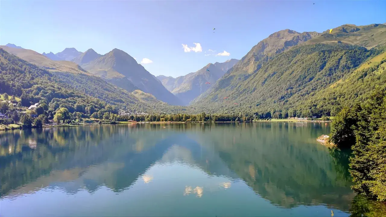 Tranquilo lac de Genos con montañas verdes y paracaidistas en el cielo azul.
