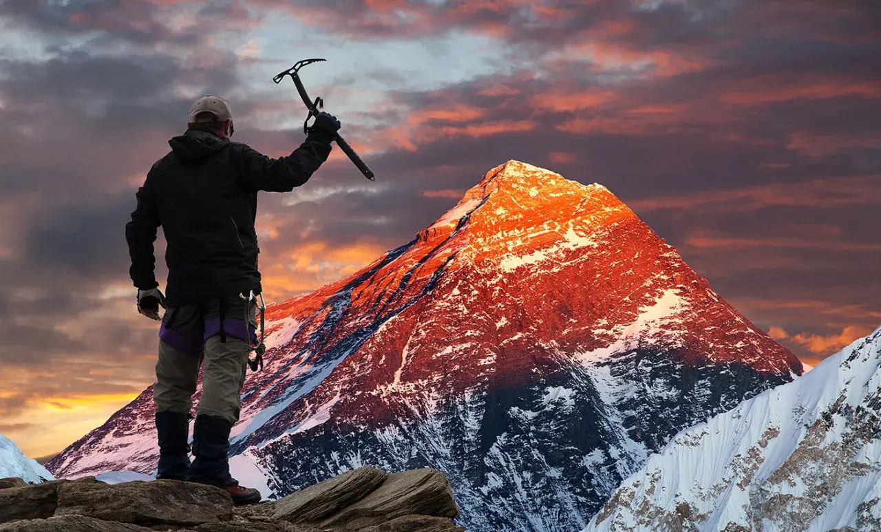 Erik Weihenmayer, escalador, levanta su piolet ante un Everest anaranjado al amanecer.