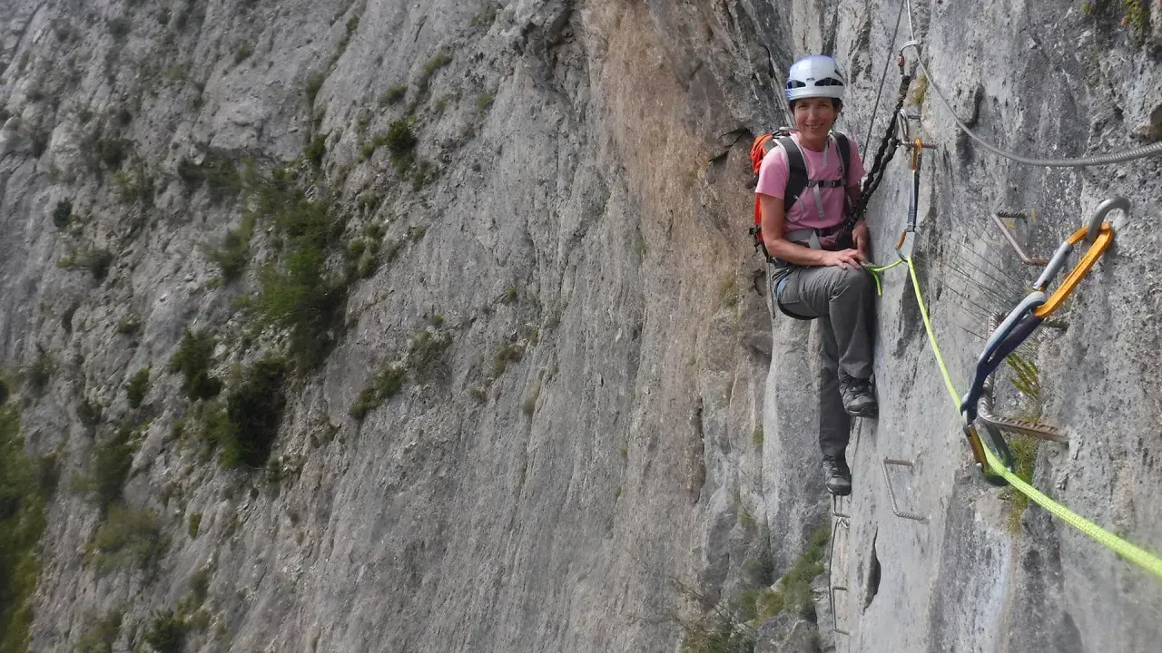 Mujer sonríe en una vía ferrata, disfrutando de la escalada en Benasque.