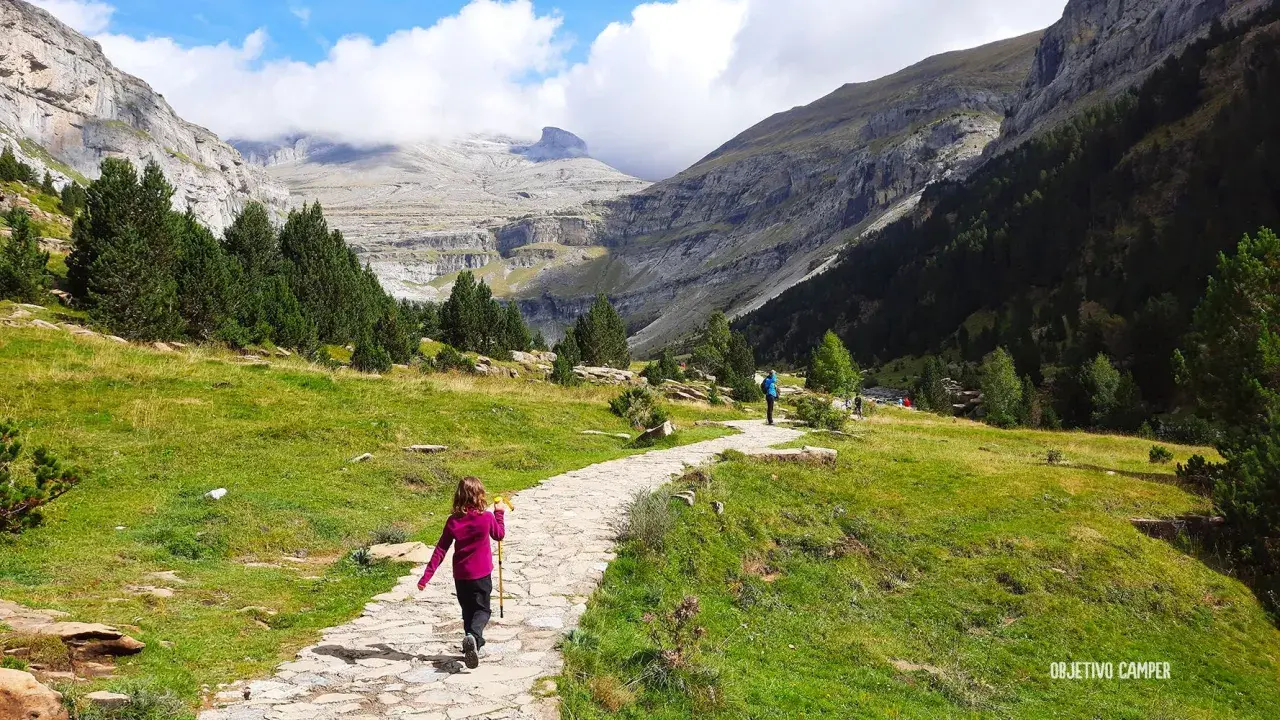 Niños disfrutan de la ruta Cola de Caballo, un camino de piedra serpentea entre prados verdes y montañas imponentes.