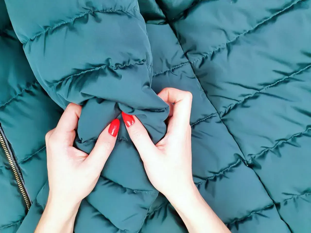 Manos con uñas rojas arrugan una chaqueta verde oscuro recién lavada.
