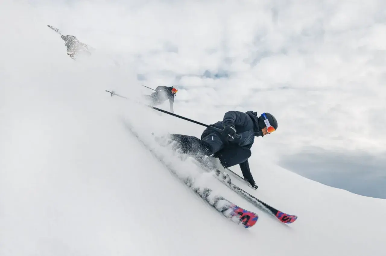 Dos esquiadores disfrutan de un descenso vertiginoso en esqui alpino, levantando nieve en su camino.
