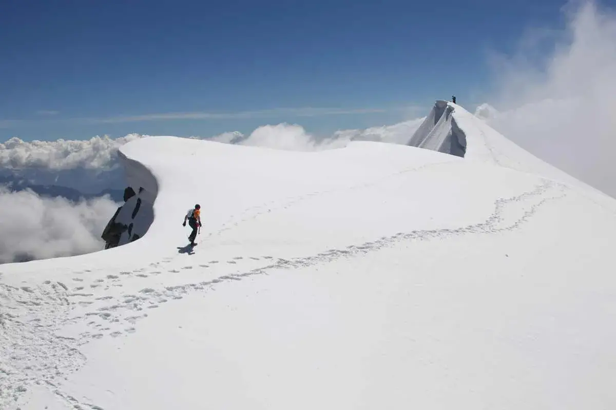 Dani Arnold camina por una cresta nevada, dejando huellas en el camino hacia la cima.