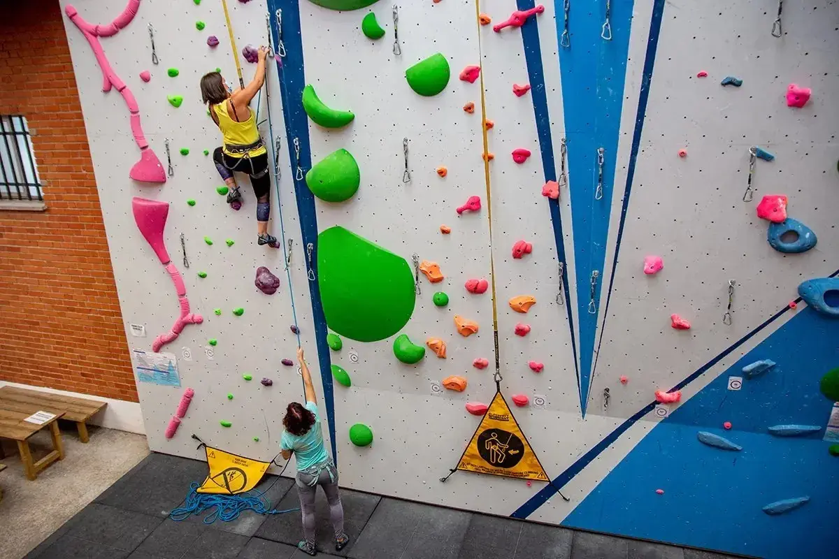 Dos escaladoras practican en un rocódromo, un muro artificial con presas de colores para trepar.