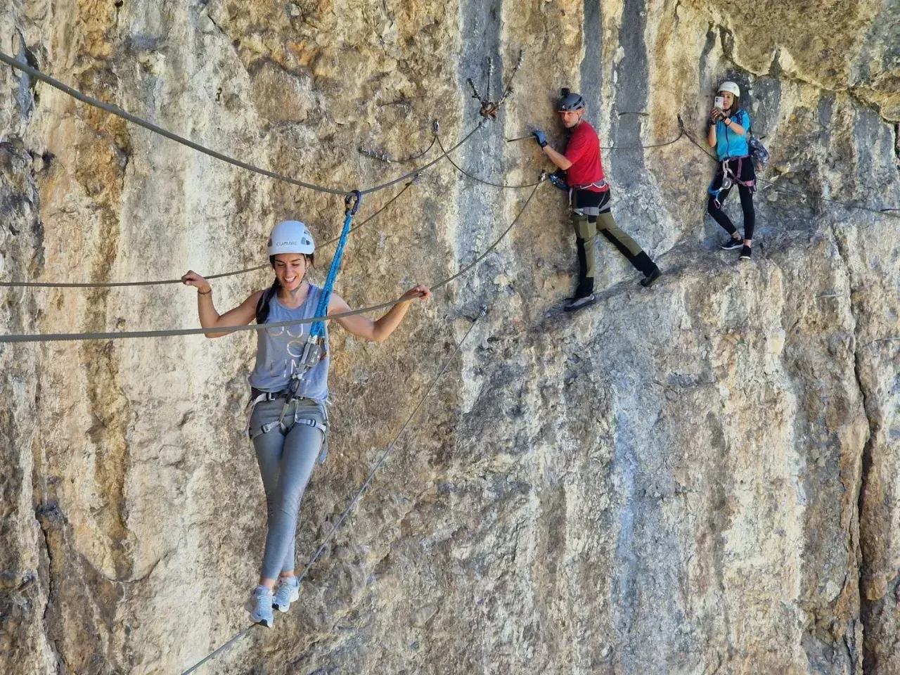 Tres personas disfrutan de una emocionante escalada con cuerda en una pared rocosa.