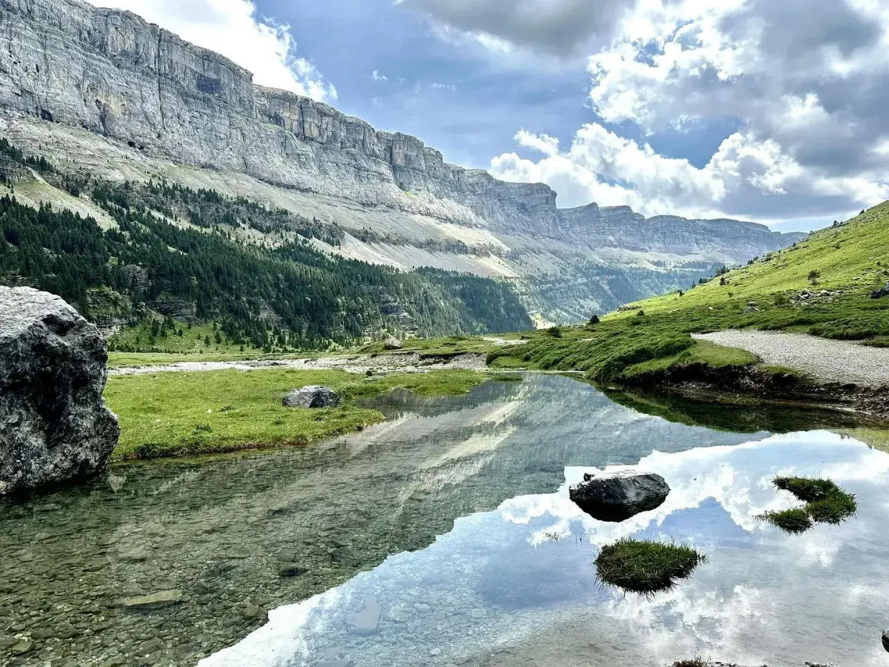 Un lago sereno refleja las imponentes montañas y el cielo nublado en el Parque Nacional de los Pirineos.