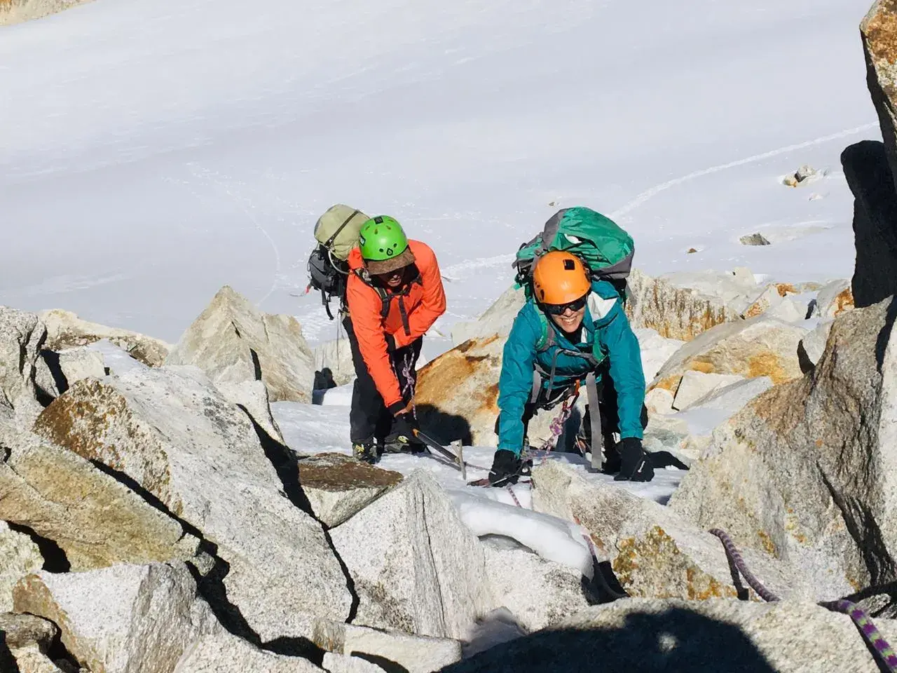 Dos escaladores con mochilas y cascos navegan por rocas y nieve en la montaña. Sus aventuras son como libros abiertos de la naturaleza.