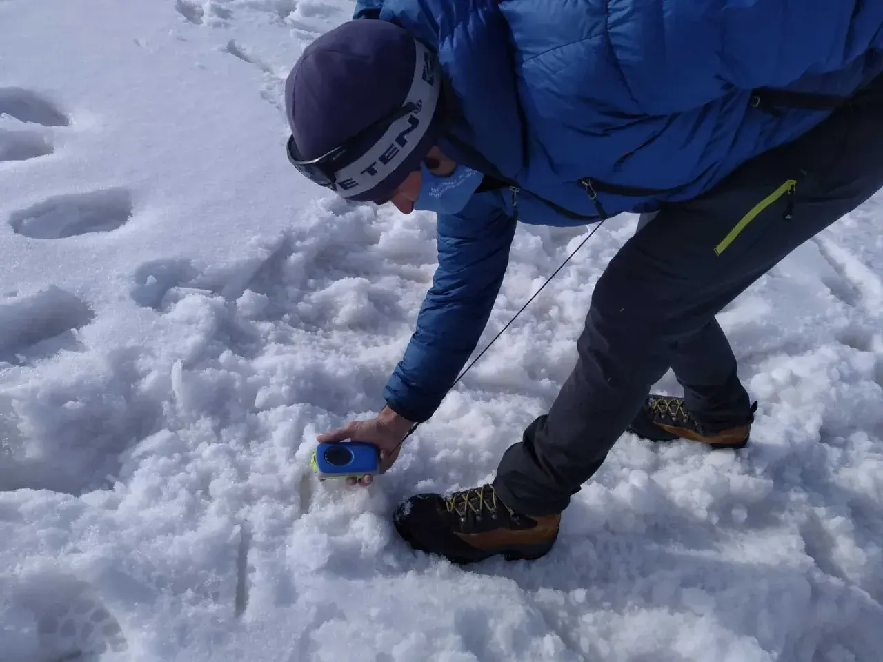 Persona en la arva montaña, con equipo de rescate, buscando algo en la nieve.