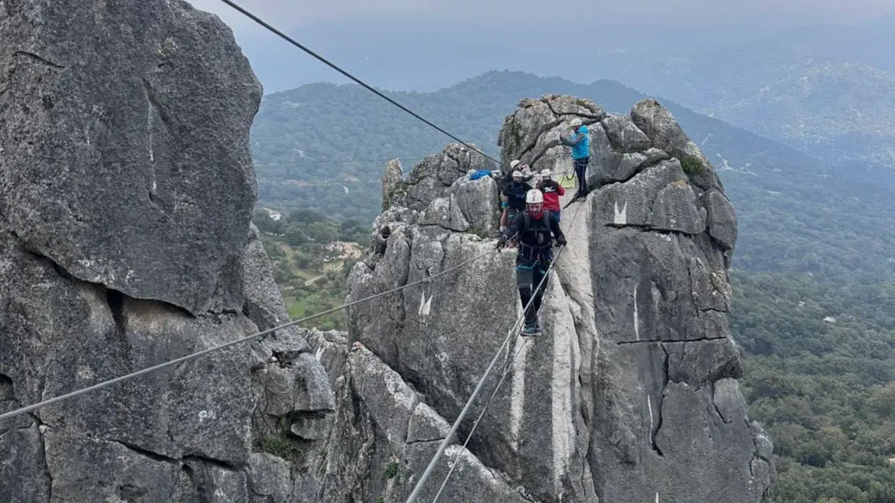 Grupo de personas superando diferentes niveles de vía ferrata, asegurados a cables de acero sobre rocas escarpadas.