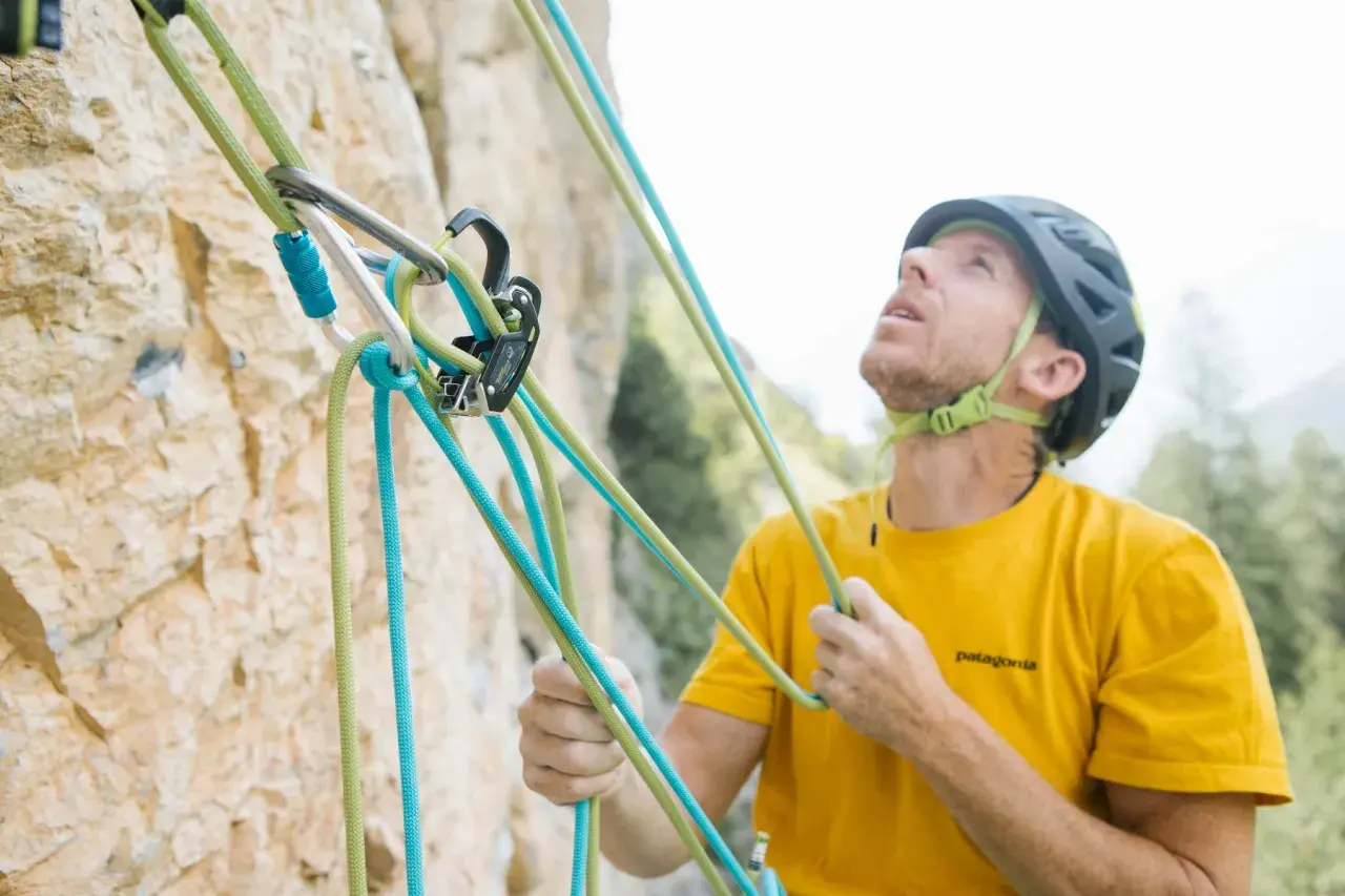 Escalador con casco y camiseta amarilla, asegurando cuerdas de escalada. La **cesta escalada** está lista para la aventura.