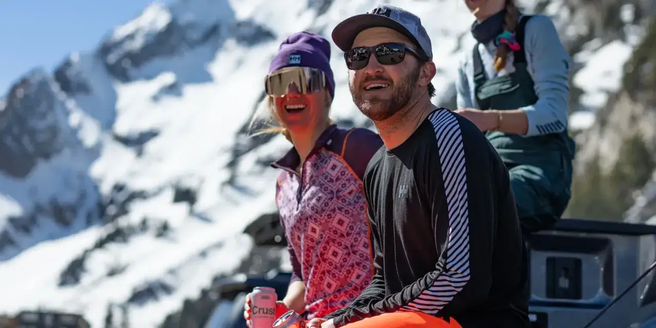 Dos amigos disfrutan del sol en la montaña, abrigados con ropa de poliamida.
