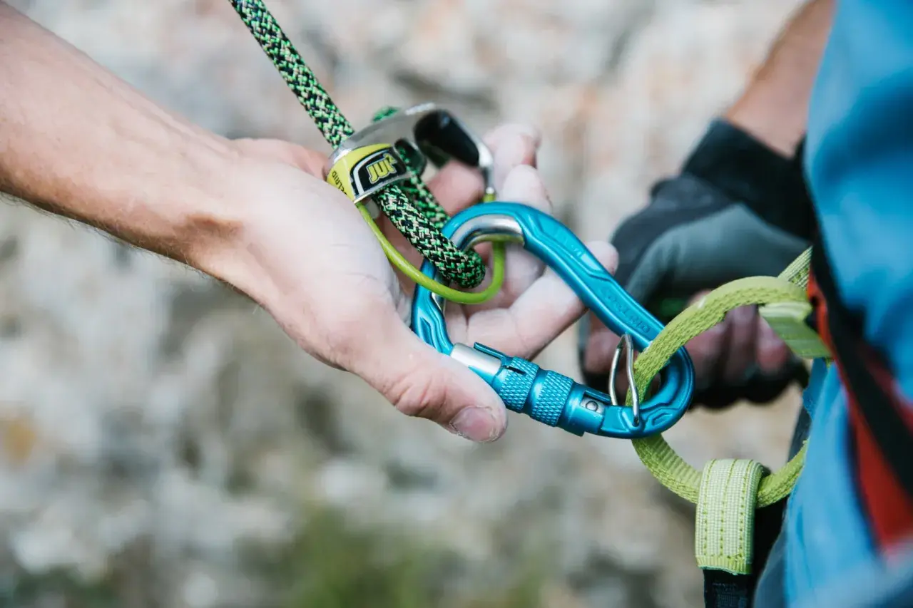 Manos ajustando cuerda y mosquetones azules, esenciales para escalada. Los mejores mosquetones garantizan seguridad.
