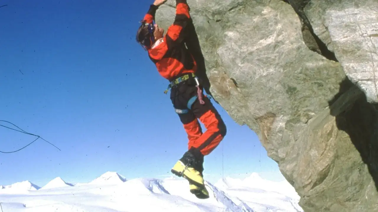Alex Lowe, escalando una roca con un paisaje nevado de fondo.