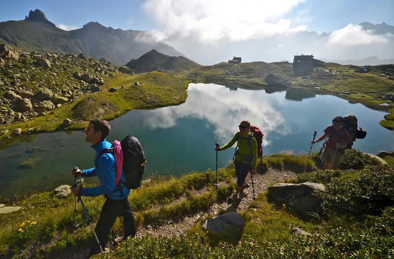 Senderistas disfrutan de la serena belleza del lac de Genos, con montañas reflejándose en sus aguas.