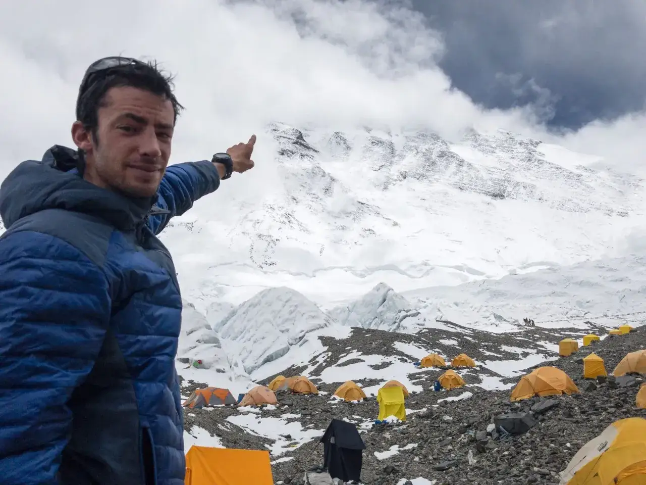 Kilian señalando la cima del Everest, rodeado de tiendas de campaña en el campamento base.