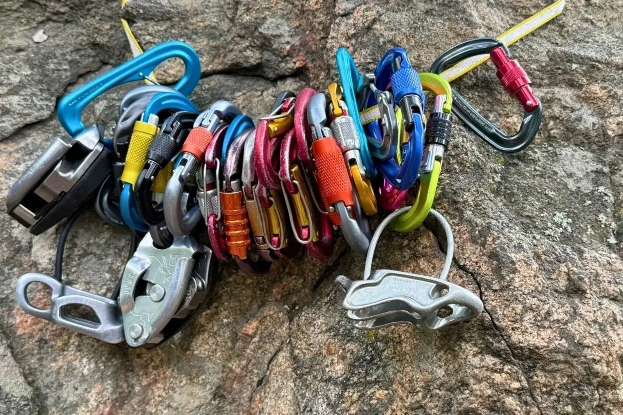 Un conjunto de mosquetones de escalada de colores vibrantes y dispositivos de aseguramiento descansan sobre una roca. Estos son los mejores mosquetones para tu próxima aventura.