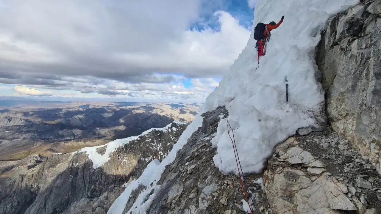 Escalador en hielo desafía la montaña, con un bru busom de nieve y roca bajo un cielo nublado.