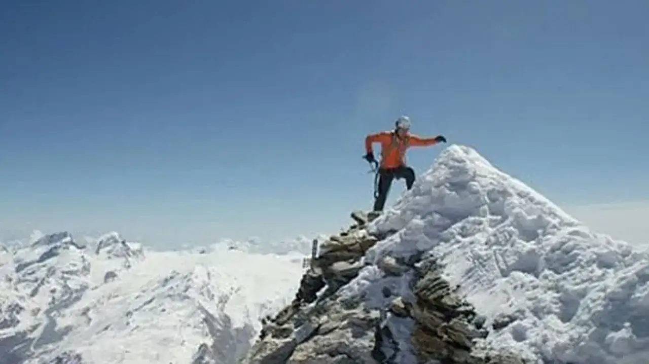 Alpinista en la cima nevada, alcanzando un nuevo récord en el Cervino. El cielo azul y las montañas heladas lo rodean.