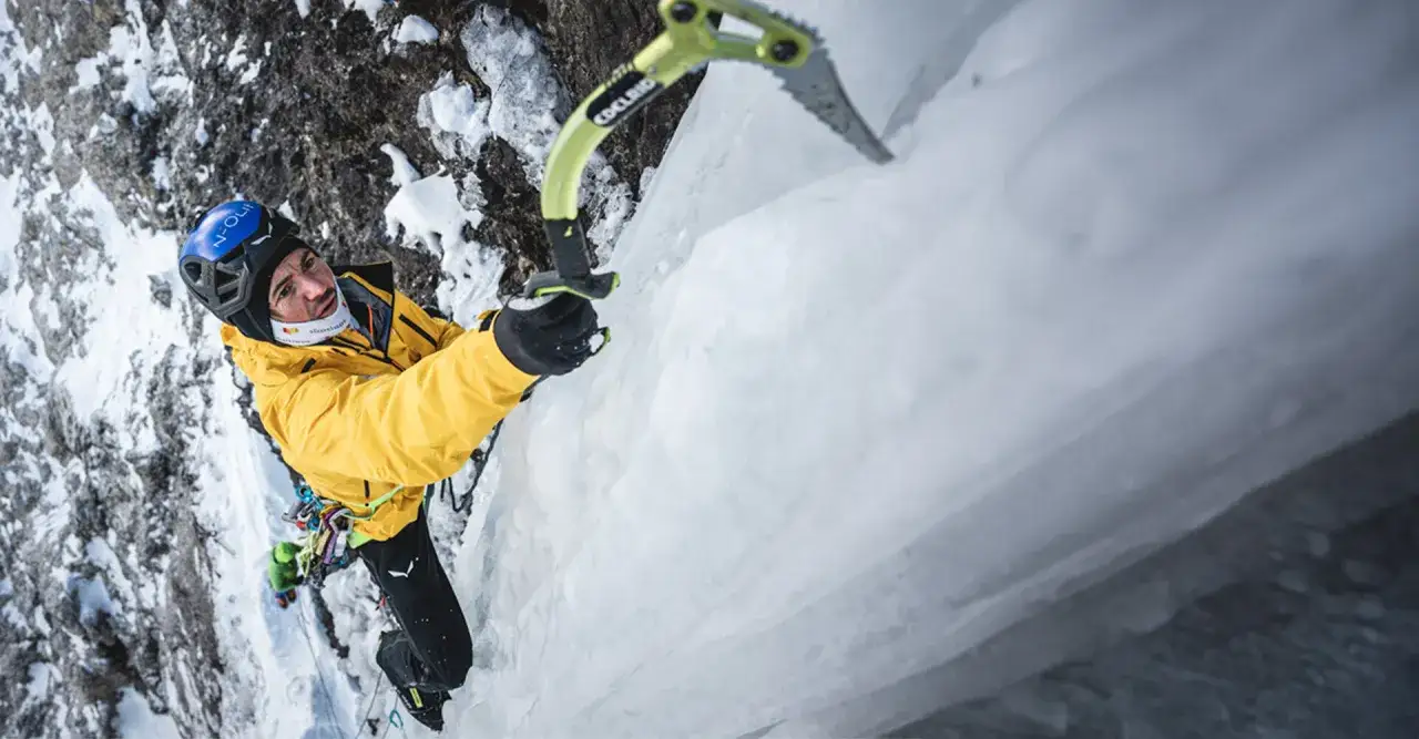 Alpinista en pared de hielo, usando piolet y equipo de escalada, con los mejores crampones para conquistar la montaña.