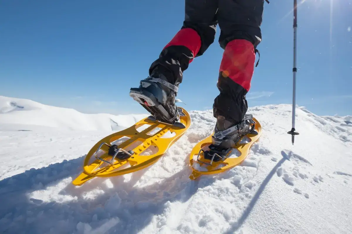 Persona camina con raquetas de nieve amarillas sobre un paisaje nevado, explorando nuevas rutas.