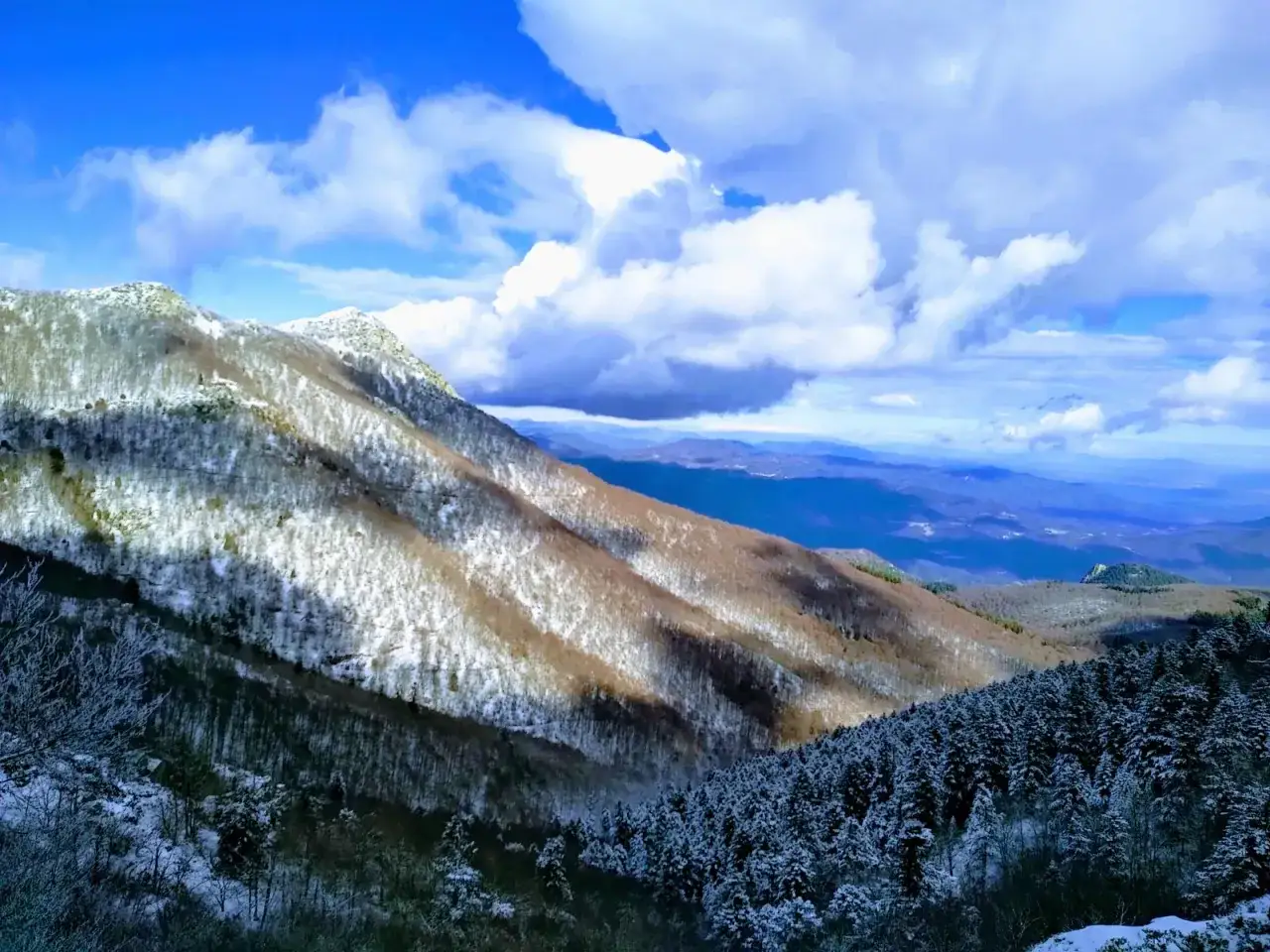 Paisaje invernal en el Montseny con nieve cubriendo las laderas y un cielo azul con nubes.