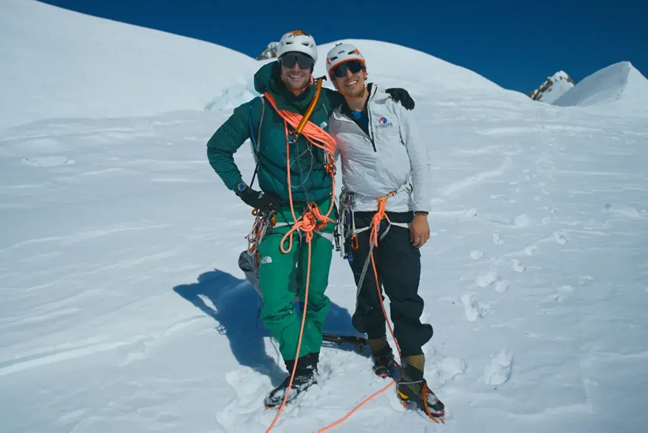 Benjamin Vedrines y compañero sonríen en la cima nevada, listos para la aventura.