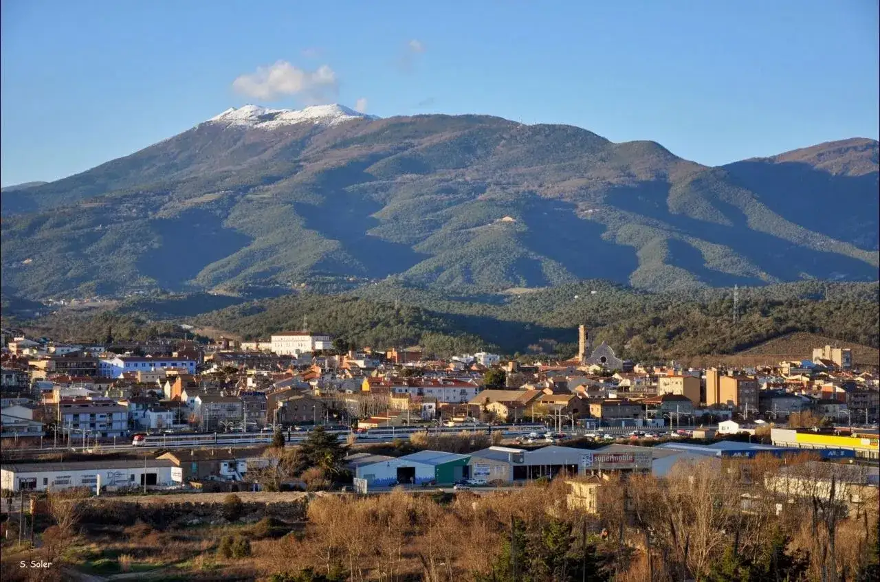 Vista de un pueblo con un turo del home nevado al fondo. El sol ilumina las casas y la vegetación.