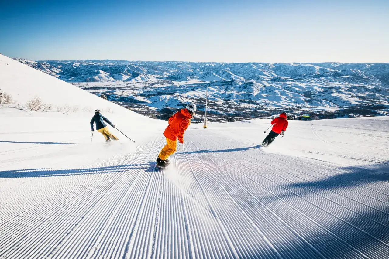 Esquiadores disfrutan de diferentes tipos de ski en una pista impecable con montañas nevadas de fondo.