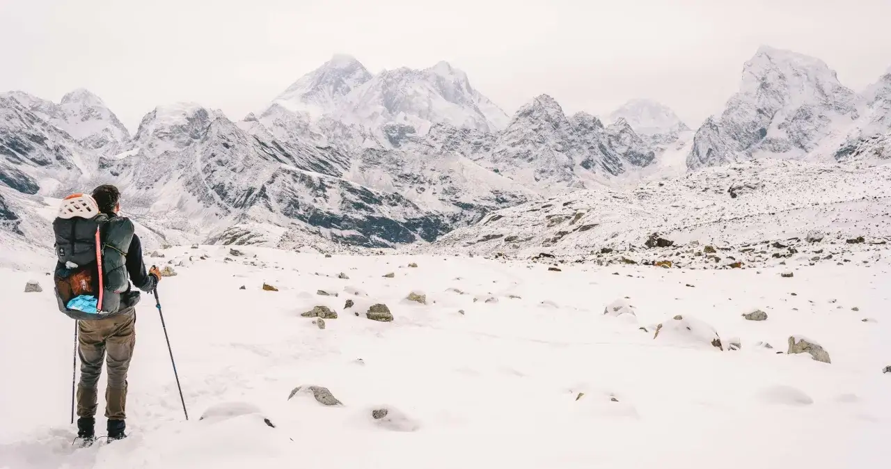 Un excursionista con mochila y bastones se enfrenta a majestuosas monta&ntilde;as nevadas, listo para el trekking himalaya.