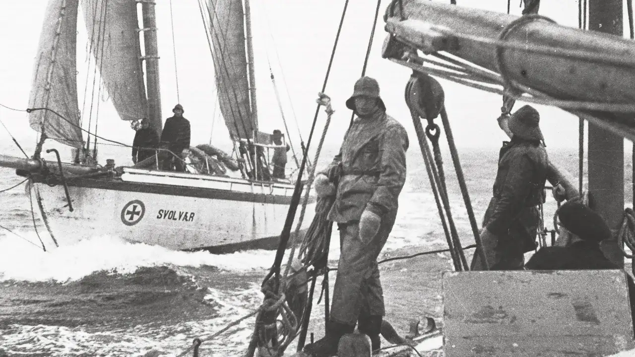 Hombres en cubierta de un barco pesquero, parte de la helly hansen historia, con velas desplegadas y el mar agitado.