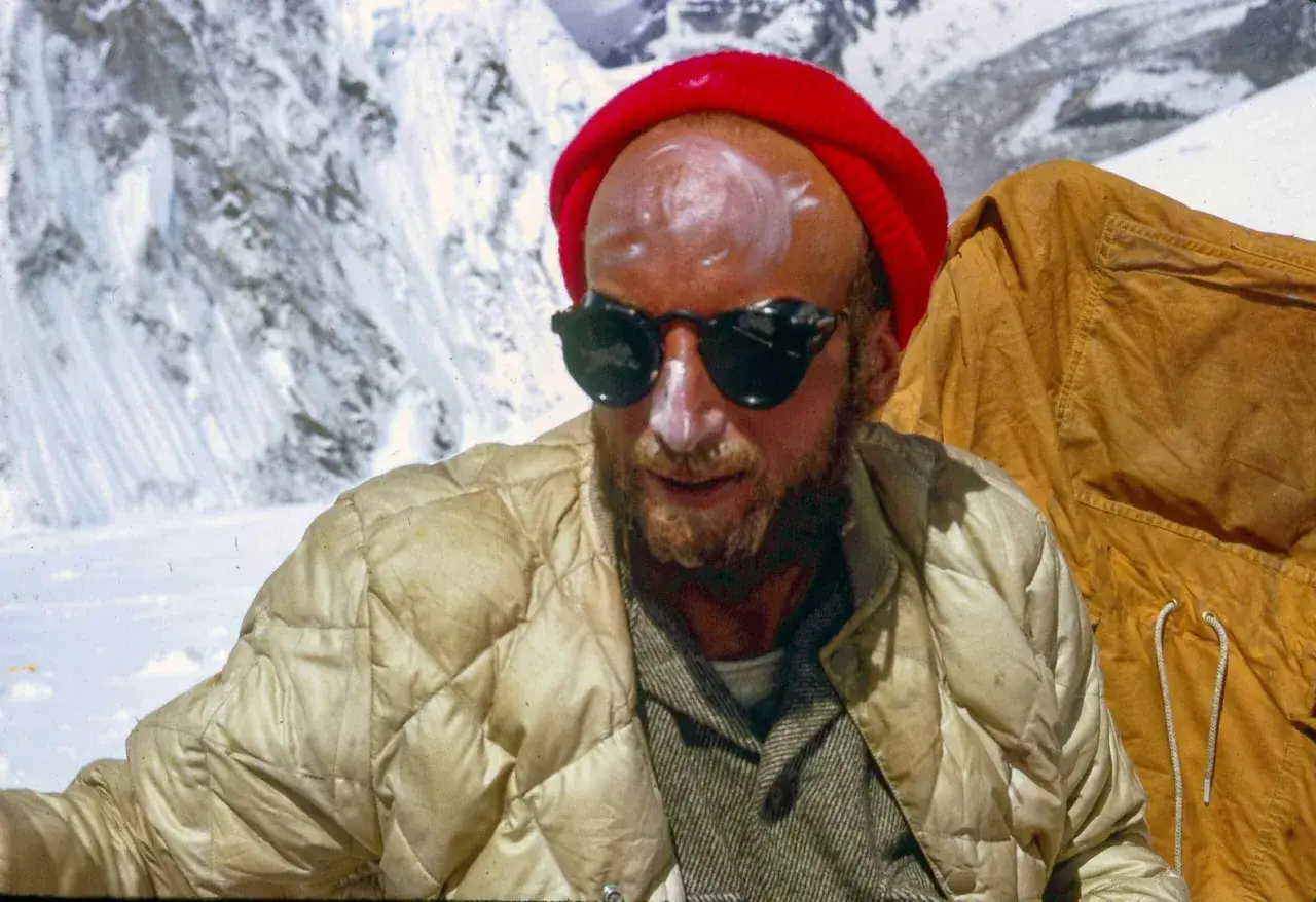 Tom Hornbein, con protector solar en la cara, gorro rojo y gafas de sol, en un paisaje nevado.