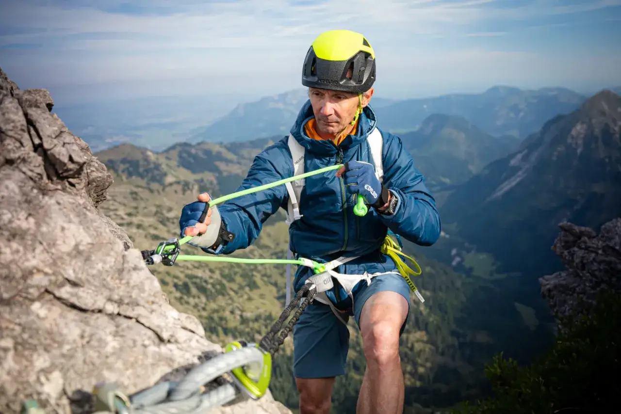Escalador con casco amarillo y equipo de seguridad, asegurando una cuerda en la montaña. Afortunadamente, no hay un accidente escalada.