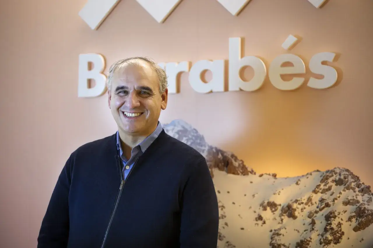 Carlos Barrabés sonríe frente a un mural de montañas nevadas y el logo de su empresa.
