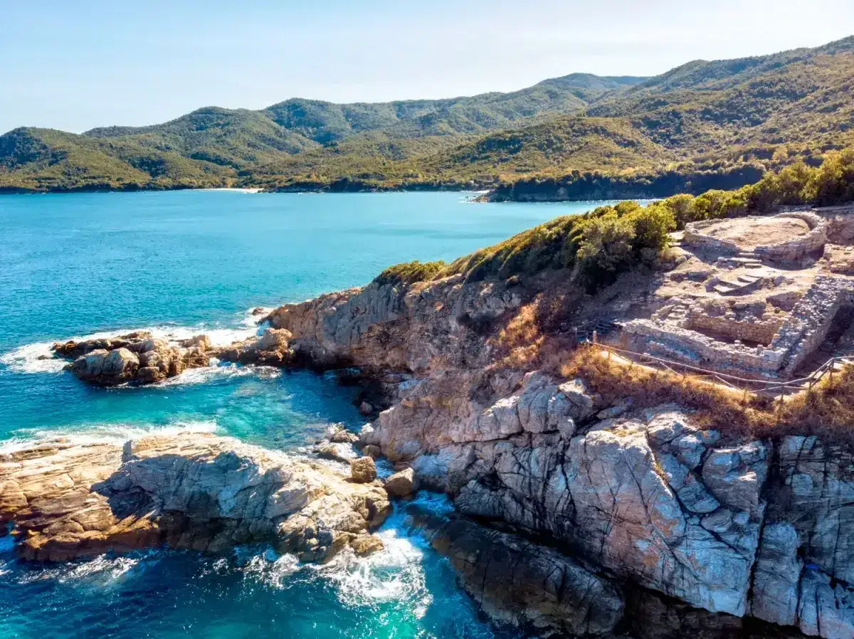 Ruinas antiguas en un acantilado rocoso con vistas al mar azul turquesa. Un sendero serpentea por la ladera, ideal para senderismo en Cataluña.