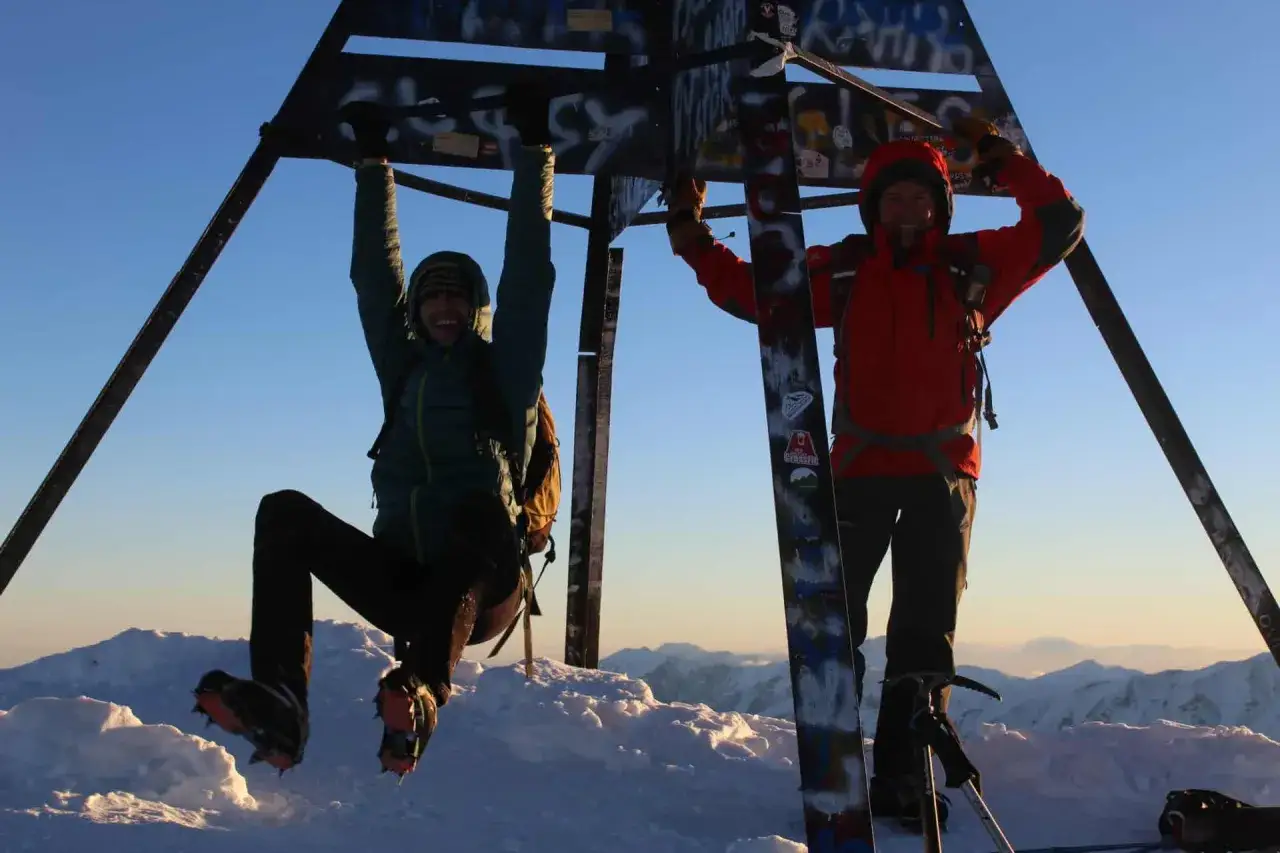 Dos alpinistas celebran en la cima del Toubkal, disfrutando de la impresionante altura y las vistas nevadas.